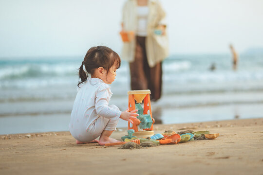 Cute Asian toddler girl playing with beach sand toys on tropical shore, happy little child enjoying summer family travel vacation and outdoor play for early childhood development concept.