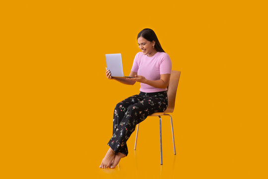 Happy Indian girl holding laptop and laughing while sitting on chair