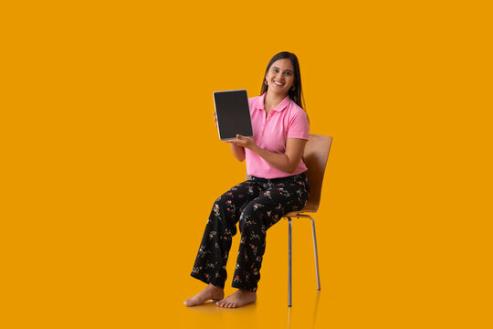 Happy Indian girl showing her tablet while sitting on chair