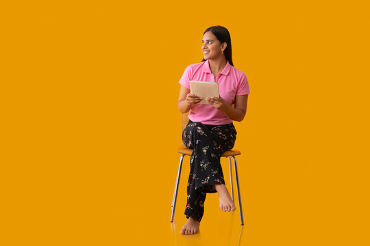 Happy Indian girl looking away while sitting on chair with holding tablet in her hand