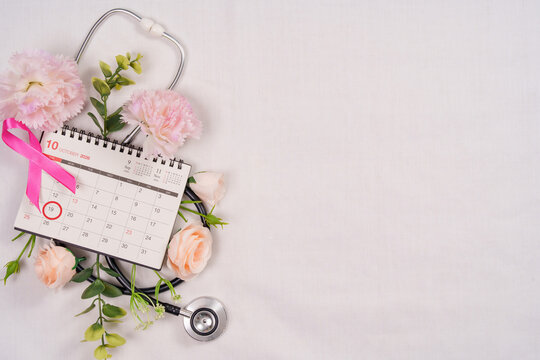 Breast cancer awareness concept with pink ribbon calendar stethoscope and flowers on white background