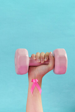 Hand holding pink dumbbell with pink ribbon for breast cancer health and fitness concept