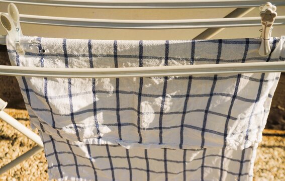 Blau-wei&szlig; kariertes Geschirrhandtuch h&auml;ngt zum Trocknen an wei&szlig;en W&auml;schest&auml;nder auf Terrasse bei Sonne am Morgen im Sommer