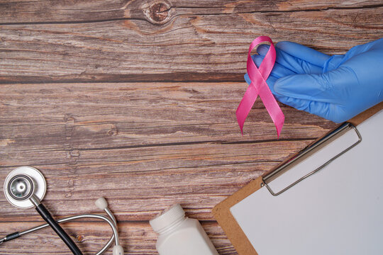 Breast cancer awareness concept with gloved doctor hand holding pink ribbon near stethoscope