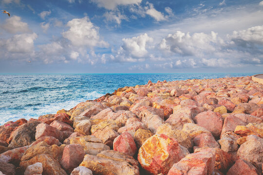 Rocky beach with red and orange stones. Seashore along Harry S. Truman Street, Tel Aviv-Jaffa, Israel