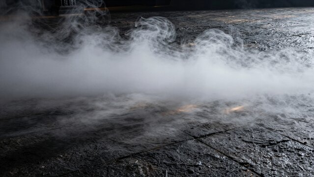White dry ice smoke drifts across a dark, wet stone surface in low light with subtle reflections.