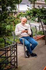 Obraz premium Mature man using a smartphone while sitting on a park bench in the city