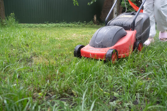 Low angle view of red lawn mower crossing overgrown garden grass