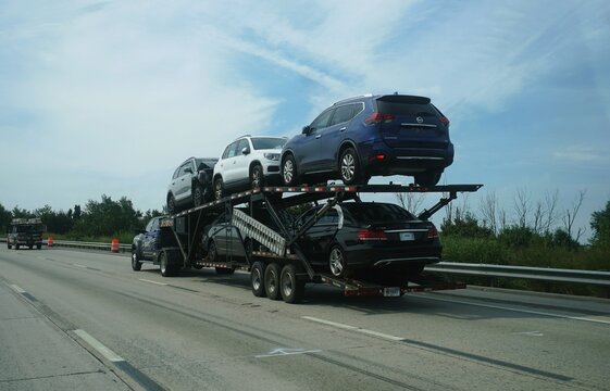 Delaware, U.S.A - Aug 1, 2026 - Car carrier trailer hauling multiple vehicles, including Nissan SUVs and Mercedes sedan, moving along the highway