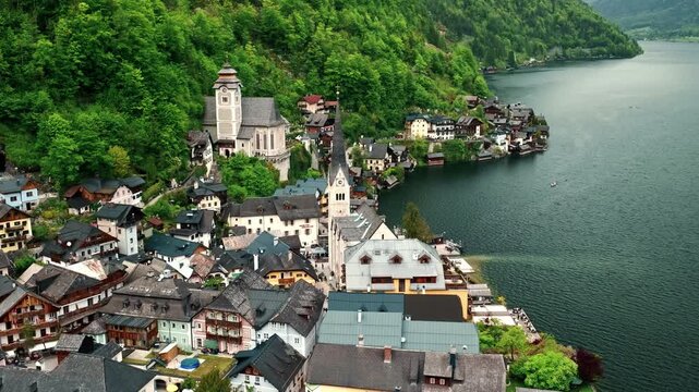 Cinematic aerial drone footage of Hallstatt surrounded by lush green forests, crystal-clear lake, and majestic Alpine mountains.