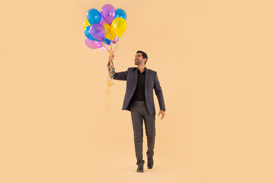 Happy businessman in formal outfit holding a bunch of balloons