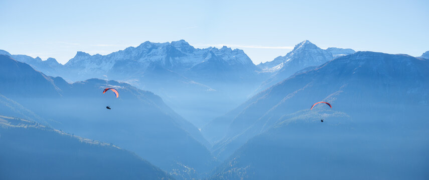 Paragliders flying in sky against mountain range layers on sunny day. Outdoor extreme sport, recreation and mountain view concept.