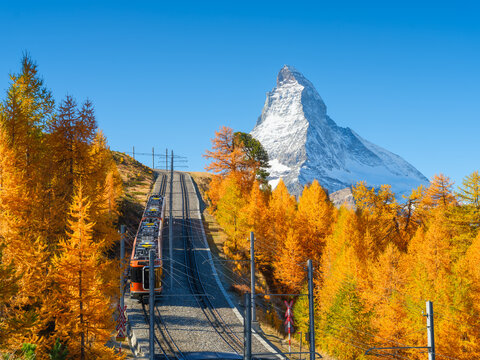Passenger train on a railway in Zermatt, Switzerland. Autumn nature in the Alps. Train passes through autumn forest with Matterhorn peak in background.