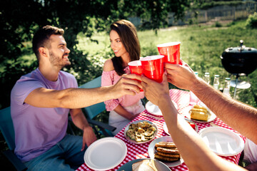 Obraz premium Friends toasting with red cups at an outdoor picnic barbecue on a sunny summer day, enjoying food and conversation in a relaxed backyard gathering