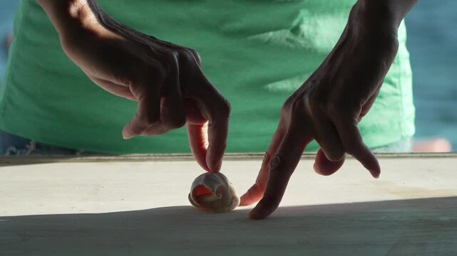 Fingers tap wooden surface near seashell by ocean backdrop in static medium shot