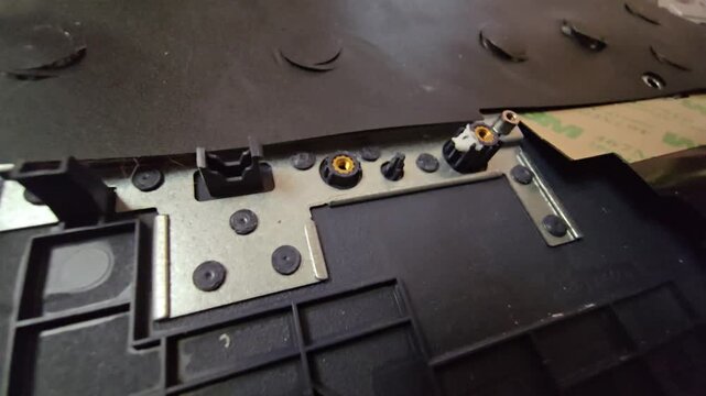Macro close-up of internal laptop plastic housing, threaded brass inserts, hinge mounts, and electronic hardware components.