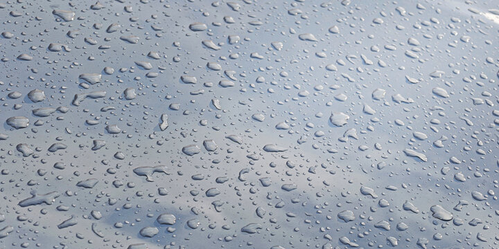 Water droplets cover a smooth, metallic surface, forming a natural pattern and reflecting light, creating a clean, wet texture