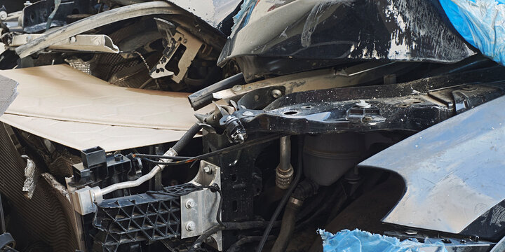 Damaged black car showing crumpled front, exposed engine components, and twisted metal, reflecting accident aftermath or vehicle dismantling