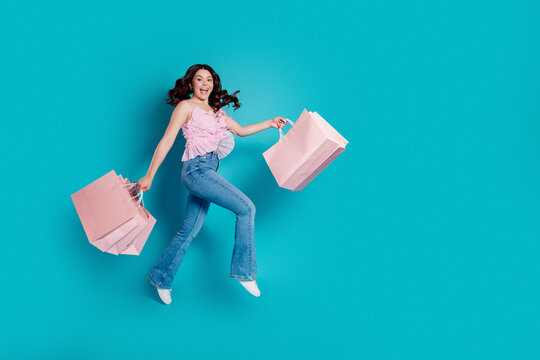 Happy young woman jumping with pink shopping bags against a turquoise background, joyful sale shopping concept, fashion style and carefree summer mood