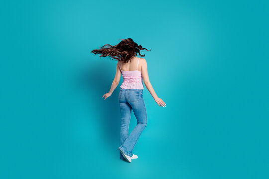 Young woman spinning in jeans and a pink top on a vibrant blue background conveying movement and joyful casual style