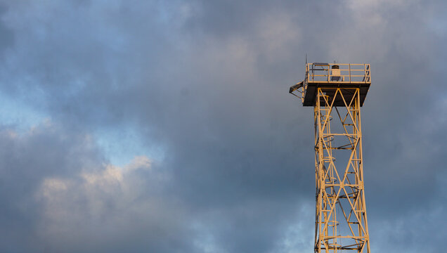 Metal watchtower structure with cloudy sky background during golden hour