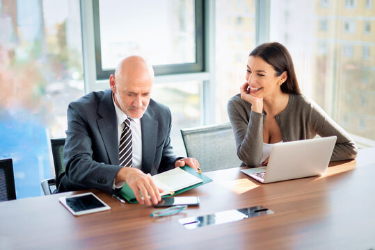 Two mid-aged business people working together on a laptop in a modern office