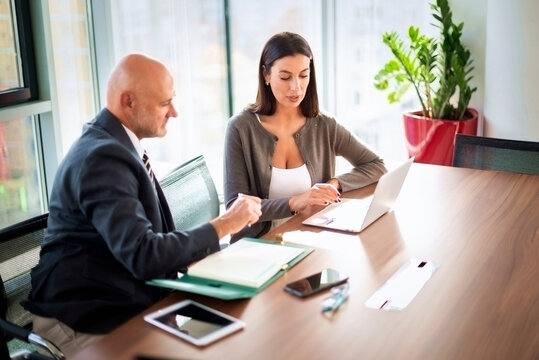 Two mid-aged business people working together on a laptop in a modern office
