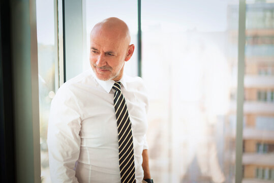 Mid-aged businessman contemplating in a modern bright office with a view of the city