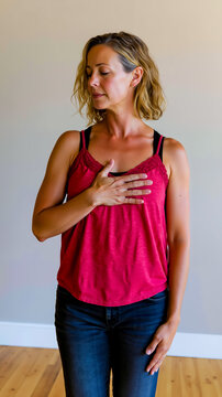 A woman in a red top with her eyes closed standing with her hands on her chest
