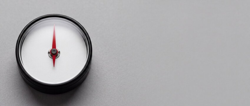 Single black navigational compass with red needle pointing north resting on plain gray surface providing simple orientation and direction