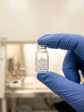Hand in Blue Glove Holding Vial of Clear Optical Microspheres