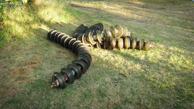 High voltage insulator string electrical transmission components on dry grass. Glass disc insulators for overhead power lines at outdoor utility maintenance storage with weathered industrial equipment