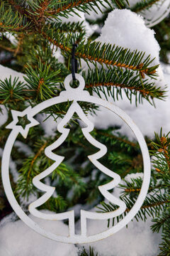A decorated Christmas tree stands covered in snow. The scene shows a metal ornament shaped like a tree hanging from the branches in a winter setting