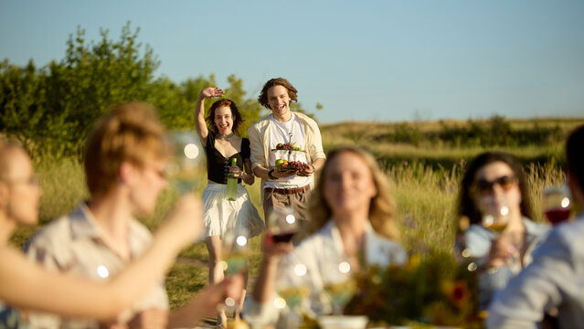 Women serving drinks and welcoming guests at elegant countryside gathering. Concept of event service, welcoming hospitality, premium outdoor catering.