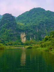 Fototapeta premium Small Boat by a Grassy Bank Beneath Karst Peaks in Ninh Binh, Vietnam