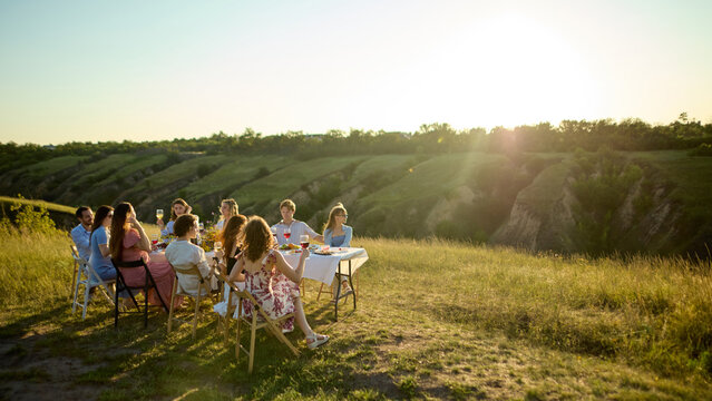 Friends gathered around outdoor dinner table in vast sunlit Riviera landscape. Concept of scenic lifestyle, resort event planning, nature-based hospitality.