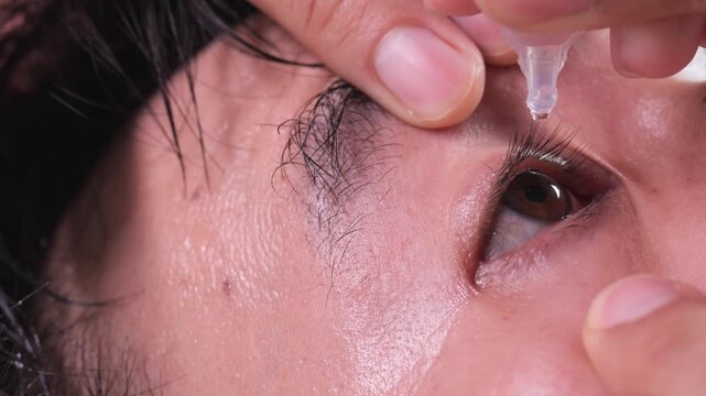 Extreme close-up of a hand applying artificial tear eye drops near the eyelid and eyelashes, demonstrating proper eye care technique.	