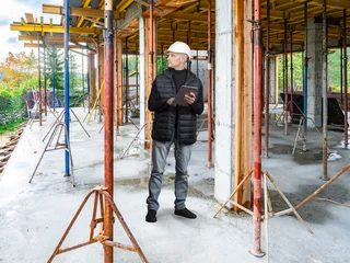 Construction Site. Construction engineer performs structural inspection and supervises reinforced concrete building works using a tablet during on site project management. © Grispb