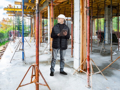 Construction Site. Construction engineer performs structural inspection and supervises reinforced concrete building works using a tablet during on site project management.