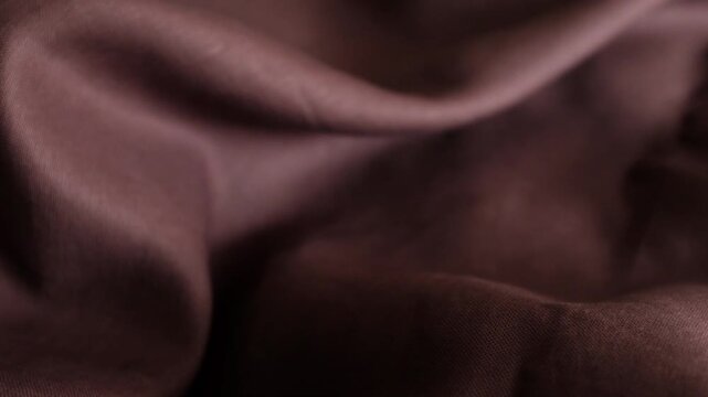 A high-detail, close-up shot moves across draped brown fabric, showcasing its fine weave and soft, elegant folds. For background textures, fashion design presentations, textile industry