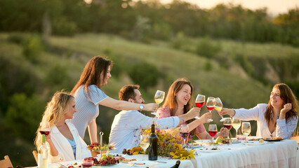 Obraz premium Women reaching across outdoor table to clink wine glasses in celebration. Concept of female community, friendship campaign, celebratory beverage marketing.