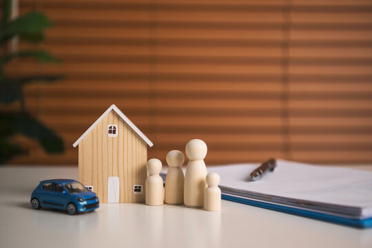 Family insurance planning with wooden house car and figurines beside policy documents representing financial protection asset coverage security and future stability.