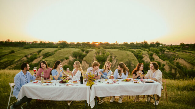Panoramic view of friends celebrating around long table in green Riviera countryside. Concept of team retreat, resort venue promotion, shared group achievement.