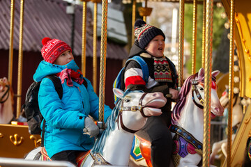 Kids enjoy a ride on a carousel at a fair in autumn while wearing warm clothing and hats © Светлана Лазаренко