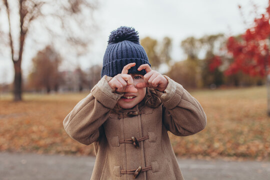 Cute little girl making frame shape with her hands to pretend she is taking photo in autumn park. Joyful child playing outdoors, exploring world with creativity and imagination during autumn season.