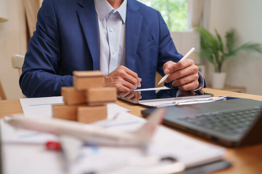 Businessman managing logistics on tablet with shipment documents and cargo boxes, supporting supply chain planning.