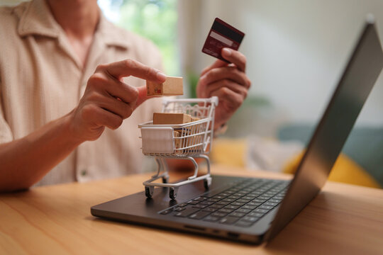Man shopping online with credit card and mini cart on laptop, highlighting secure checkout, e-commerce and delivery.