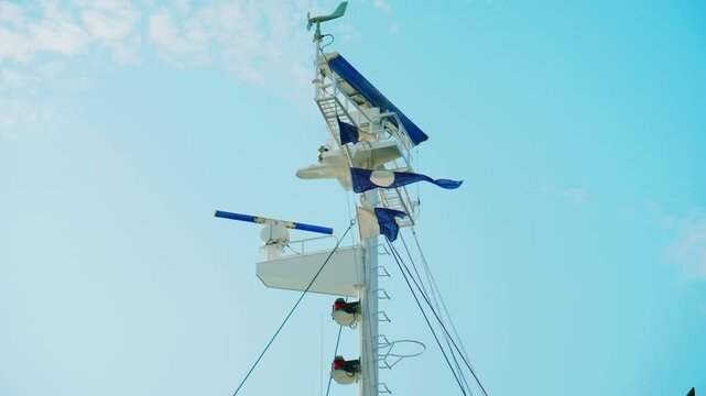 Ship Mast with Radar Antennas and Blue Flags Against Sky