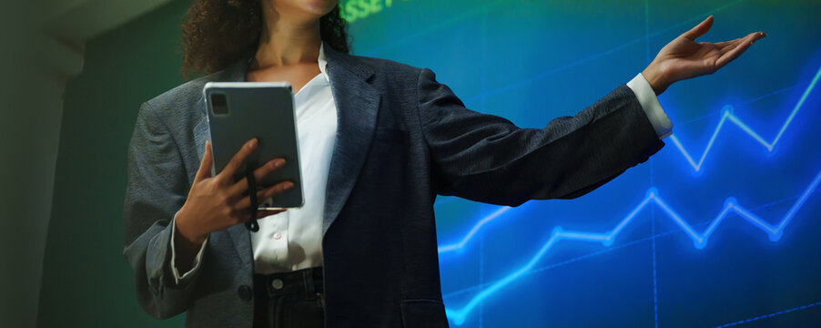 Businesswoman presenting stock market trends with tablet and financial charts, explaining investment strategy and analytics.