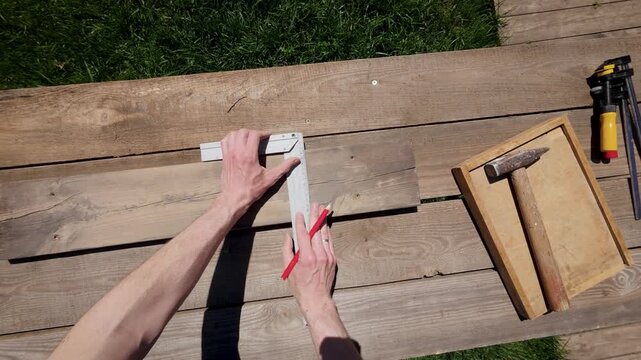 Close-up POV video of a craftsman measuring and aligning wooden boards with a try square and pencil during a DIY bird feeder construction. The first-person perspective